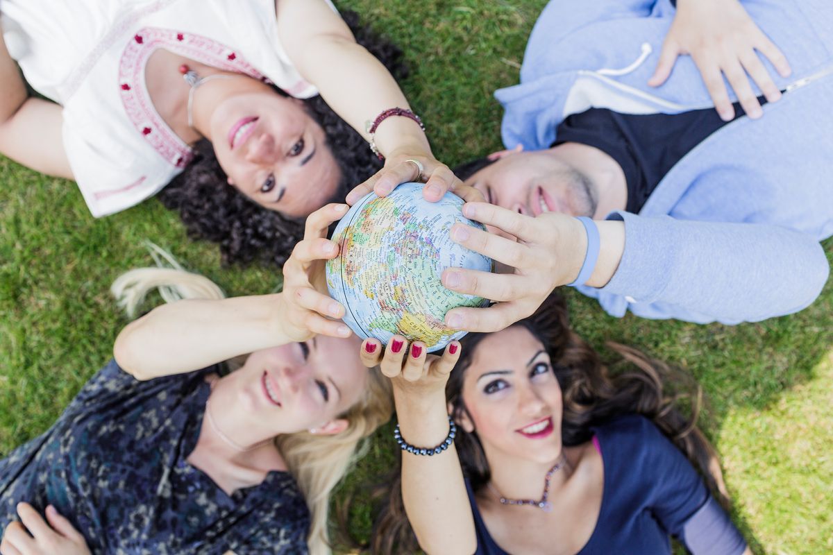 enlarge the image: Foto: vier junge Menschen liegen auf der Wiese und halten gemeinsam eine kleine Weltkugel in der der Hand