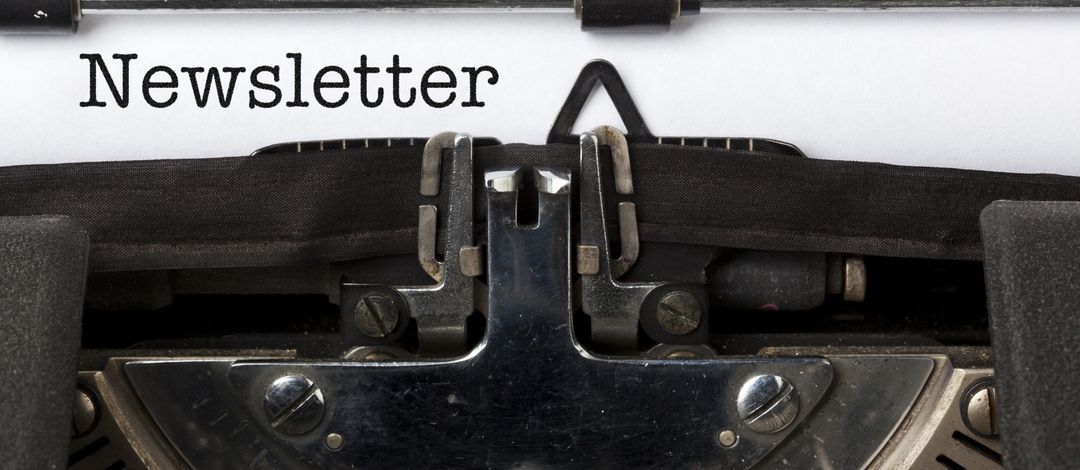 Detailaufnahme: eine alte Schreibmaschine mit Farbband, ein weißes Blatt papier ist eingespannt und es ist das Wort "Newsletter" zu lesen.