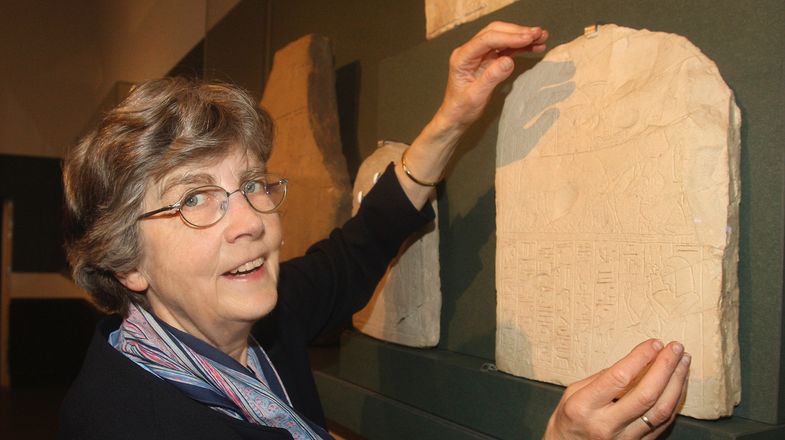 Elke Blumenthal im Museum, stehend neben einer Stele, die sie gerade mit beiden Händen berührt. Foto: André Kempner