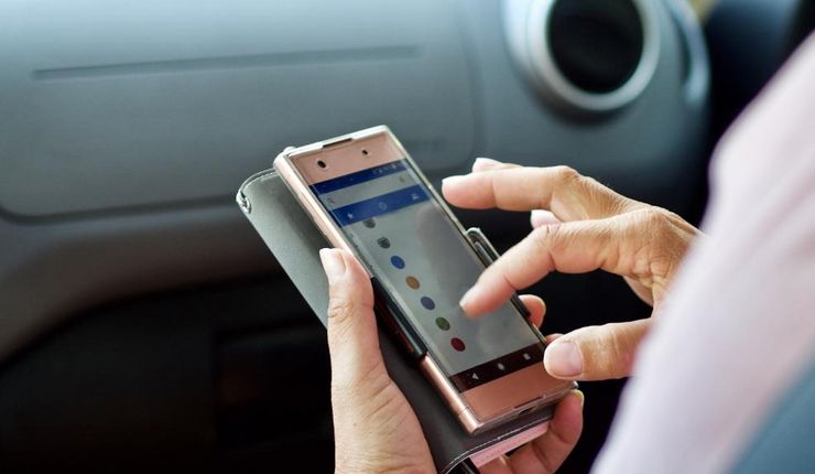 Eine Frau sitzt auf dem Beifahrersitz eines Autos, in der Hand hält sie ihr Smartphone.
