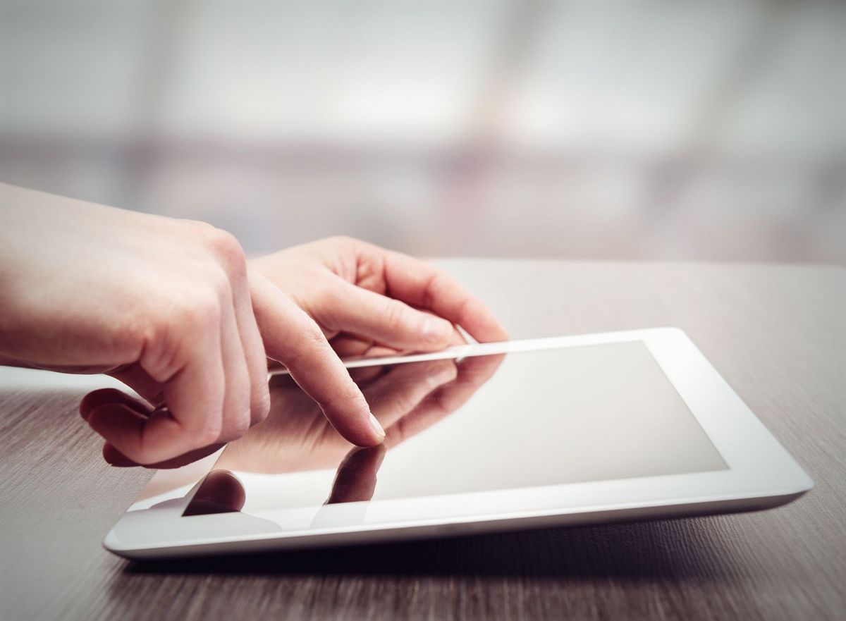 zur Vergrößerungsansicht des Bildes: Nahaufnahme eines Tablets. Eine Hand tippt darauf herum.