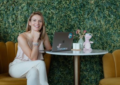 Isabell Espig, Gründerin der Onlineplattform „Rosa Krokodil“, Foto: Elena Heymann Porträt einer Frau, die an einem Tisch sitzt, auf dem ein Laptop liegt sowie ein rosa Kuscheltierkrokodil