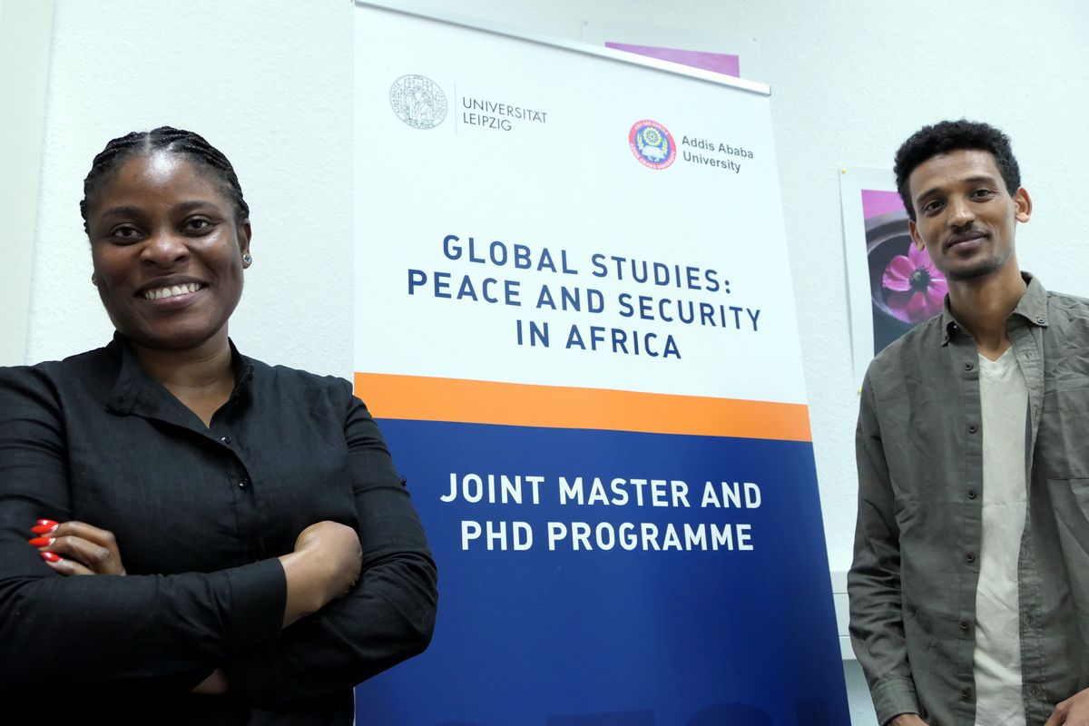 enlarge the image: Two students smile next to a banner of the joint PhD program Global Studies Peace and Security in Africa. Photo: GESI/Leipzig University