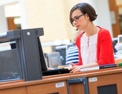 Foto: Eine junge Frau sitzt in der Universitätsbibliothek am Laptop und arbeitet.