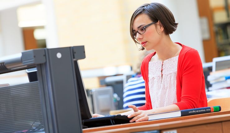 Foto: Eine junge Frau sitzt in der Universitätsbibliothek am Laptop und arbeitet.