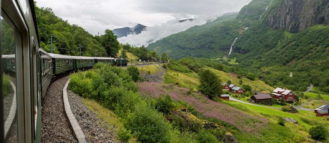 Blick aus einem fahrenden Zug auf eine bergige, grüne Landschaft.