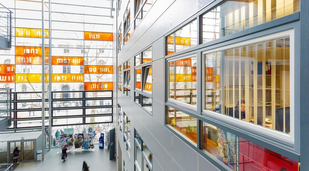 Sicht von oben auf das Foyer des Geisteswissenschaftlichen Zentrums und seiner Glassfassade mit bunten Elementen