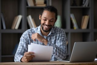 Student sitting on a desk and smiling while reading an admission letter.