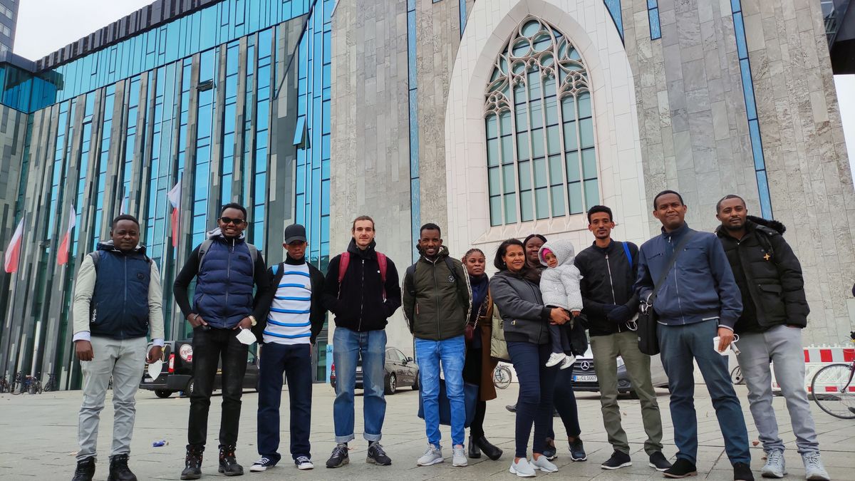 zur Vergrößerungsansicht des Bildes: Eine Gruppe von elf Studenten und ein kleines Kind posieren vor dem Hauptcampus der Universität Leipzig.