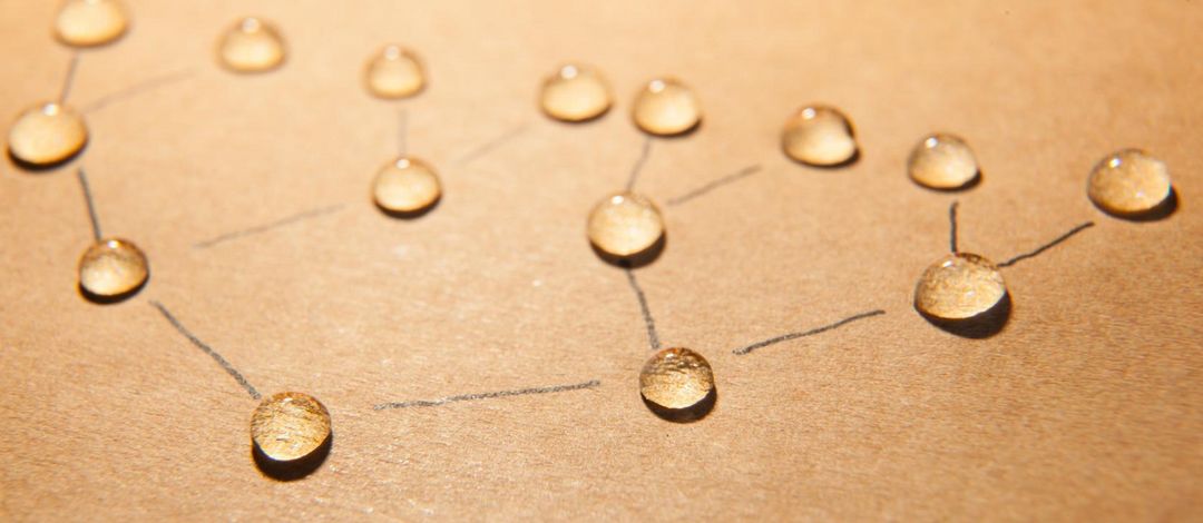 Abstrakte Darstellung von Kommunikation: Wassertropfen auf einem Blatt Papier, verbunden durch Bleistiftstriche.