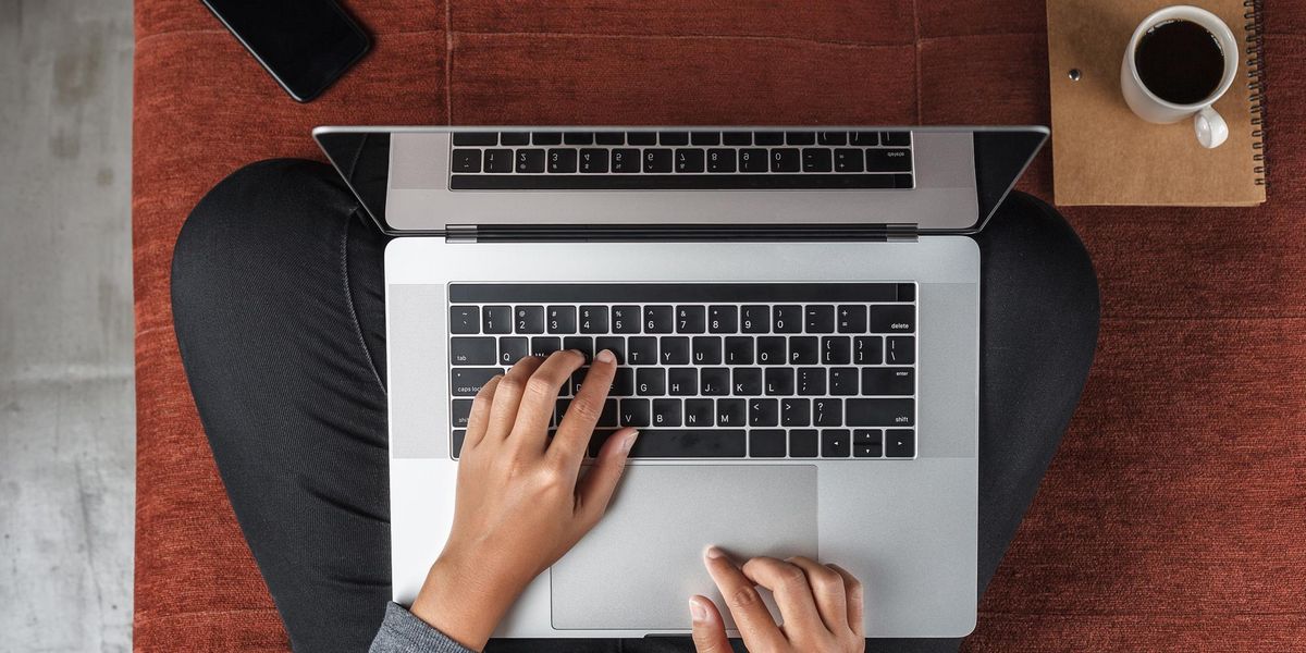 enlarge the image: Vorgelperspektive auf einen Menschen, der im Schneidersitz auf dem Fußboden sitzt. Auf dem Schoß steht der Laptop. Die Hände liegen auf der Tastatur und tippen. Der Rest vom Körper ist nicht zu sehen.