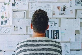 Student turning his back against the camera facing the wall and looking at a board covered with mindmaps and graphics.