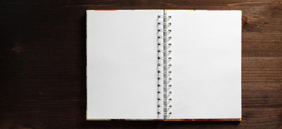 Vogelperspektive: Ein unbeschriebenes Notizbuch liegt aufgeschlagen auf einem Tisch.