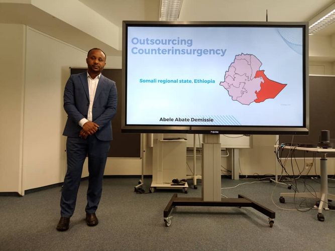 PhD student stands next to a screen with his presentation for the thesis defense. Photo: GESI
