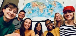 A group of seven multicultural diverse students smiling with a world map poster on the background.