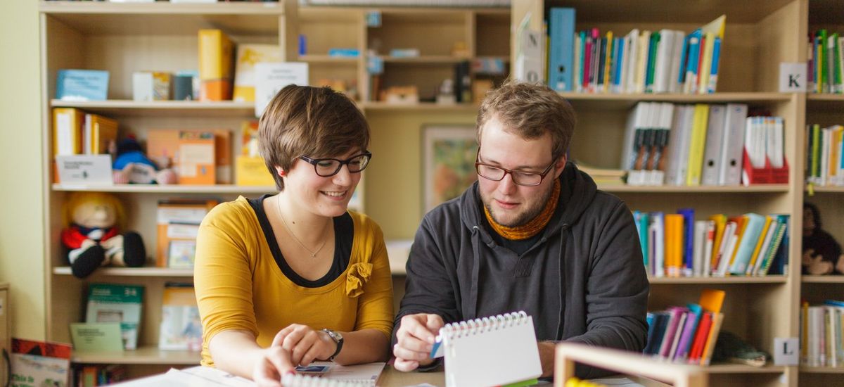 Zwei Studierende sitzen in einer Bibliothek und lernen.