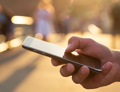 Nahaufnahme einer Hand, die ein Smartphone hält. Im Hintergrund helles Sonnenlicht.