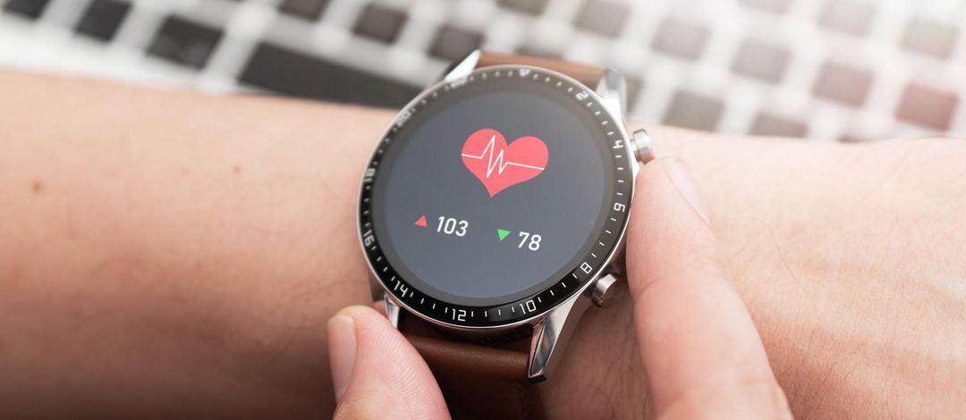 Ein Handgelenk mit einer Smartwatch. Auf dem Display wird ein rotes Herz sowie darunter die Herzfrequenz angezeigt.