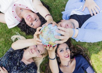 Foto: vier junge Menschen liegen auf der Wiese und halten gemeinsam eine kleine Weltkugel in der der Hand