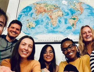 A group of seven multiculturally diverse students smiling with a world map poster on the background
