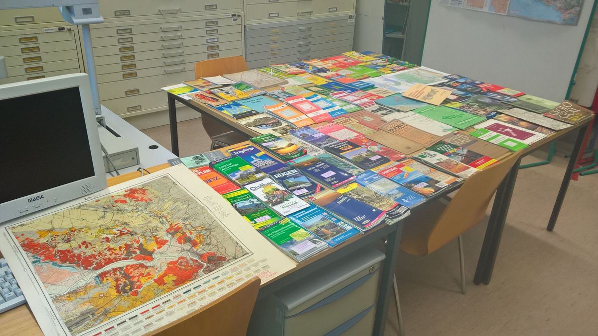 zur Vergrößerungsansicht des Bildes: Verschiedene Exemplare der Kartensammlung der Universität Leipzig auf einem Tisch ausgebreitet.