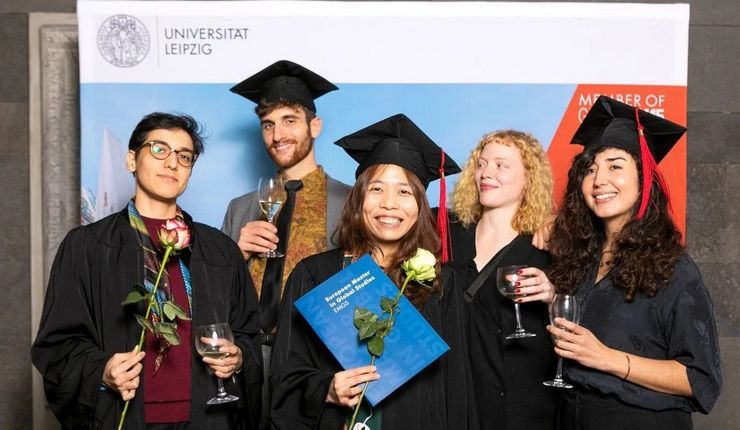 Fünf Studierenden posieren nach der Abschlussfeier mit einem Glas Wein, Blumen und ihren Diplomen.