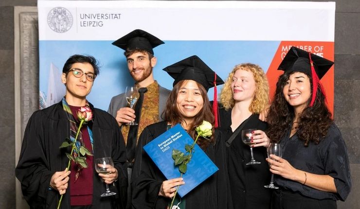 Fünf Studierenden posieren nach der Abschlussfeier mit einem Glas Wein, Blumen und ihren Diplomen.