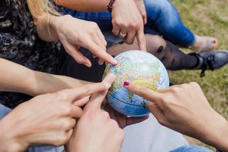 Colour photo: various hands point to a small globe