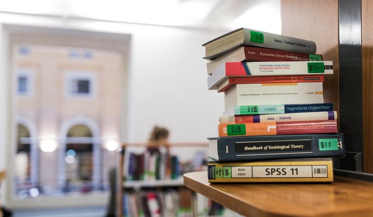 In einer Bibliohek liegen Bücher übereinandergestapelt auf dem Tisch.