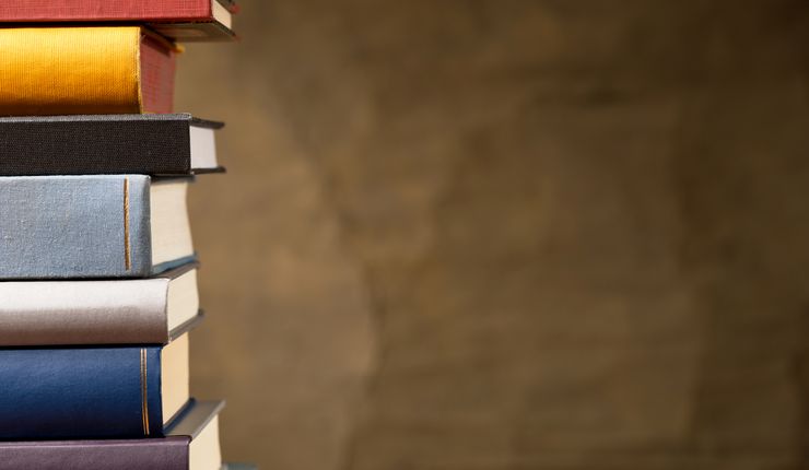 Vor einem braunen Hintergrund liegt links im Bild ein Stapel Bücher.