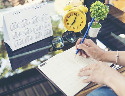 Eine Hand überträgt Termine von einem Tischkalender in einen Planer.