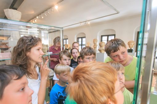 Eine Gruppe Kinder schaut interessiert in eine Vitrine des Antikenmuseums. Der Fokus liegt auf den Gesichtern der Kinder, die Exponte sind nicht abgebildet.