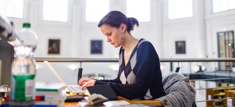 Foto: Eine Studentin sitzt an einem Arbeitsplatz in der Bibliotheca Albertina und tippt etwas in den Laptop