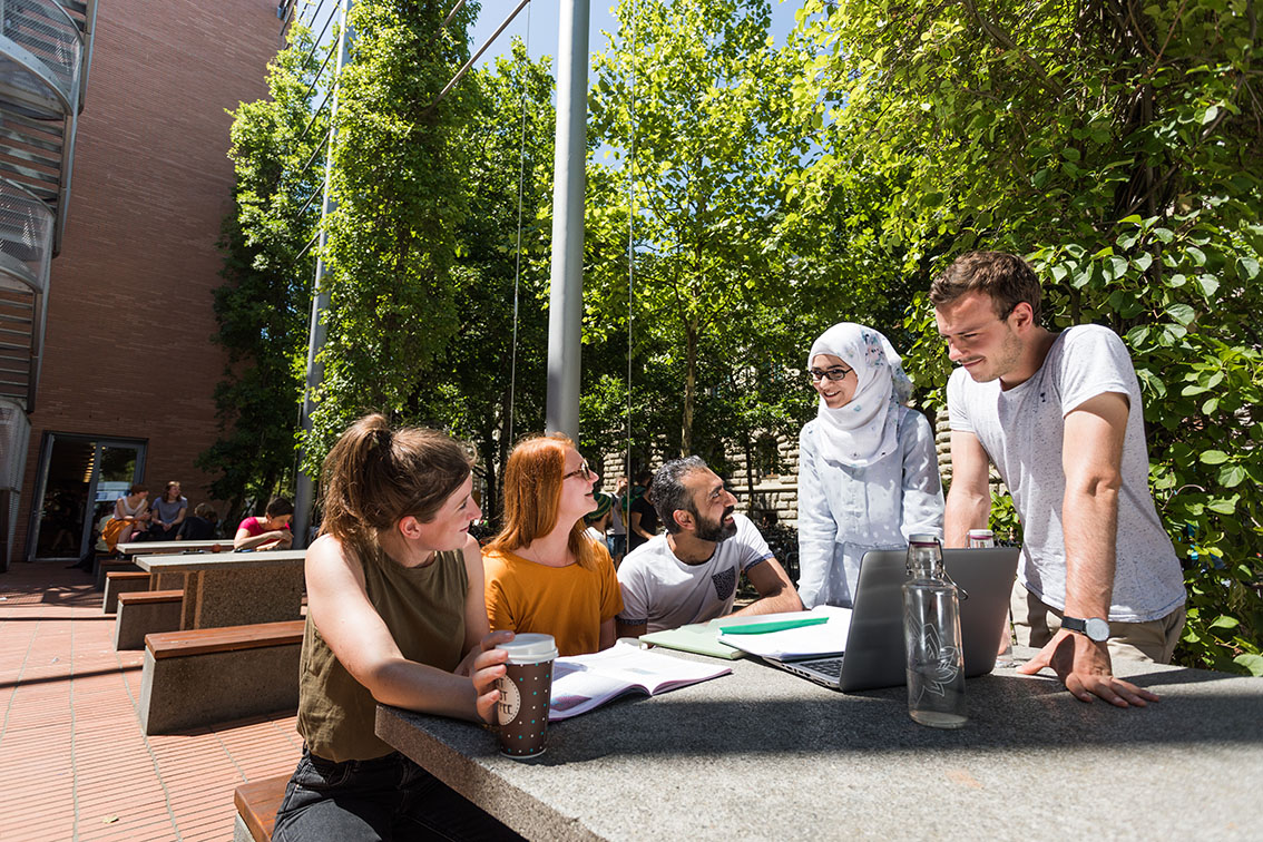 zur Vergrößerungsansicht des Bildes: Studierende unterschiedlicher Herkunft unterhalten sich vor dem Geisteswissenschaftlichen Zentrum der Universität